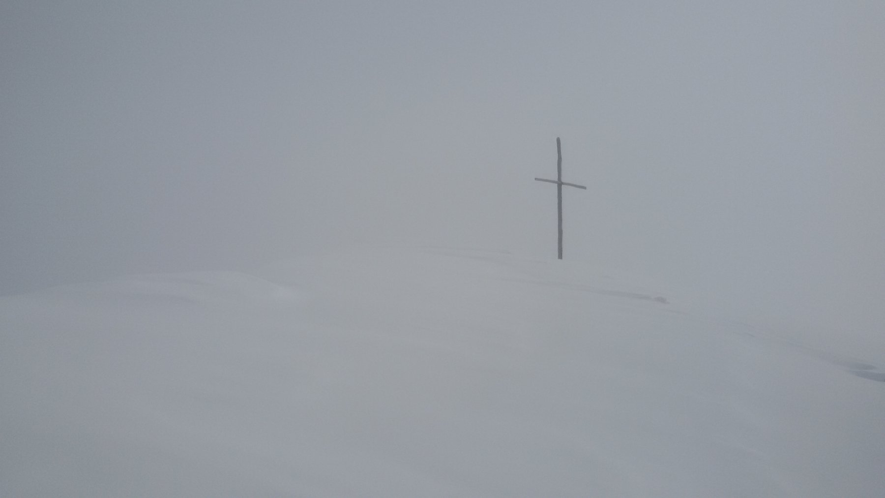 La croce di vetta emerge dalla nebbia come un fantasma 