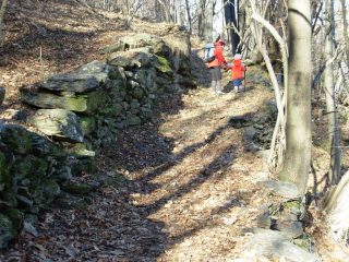 sentiero tra vecchie costruzioni ormai invase dal bosco