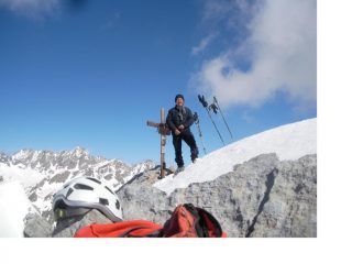 Paolo posa solo soletto a fianco della croce di vetta con al fondo l'Aig du Chambeyron