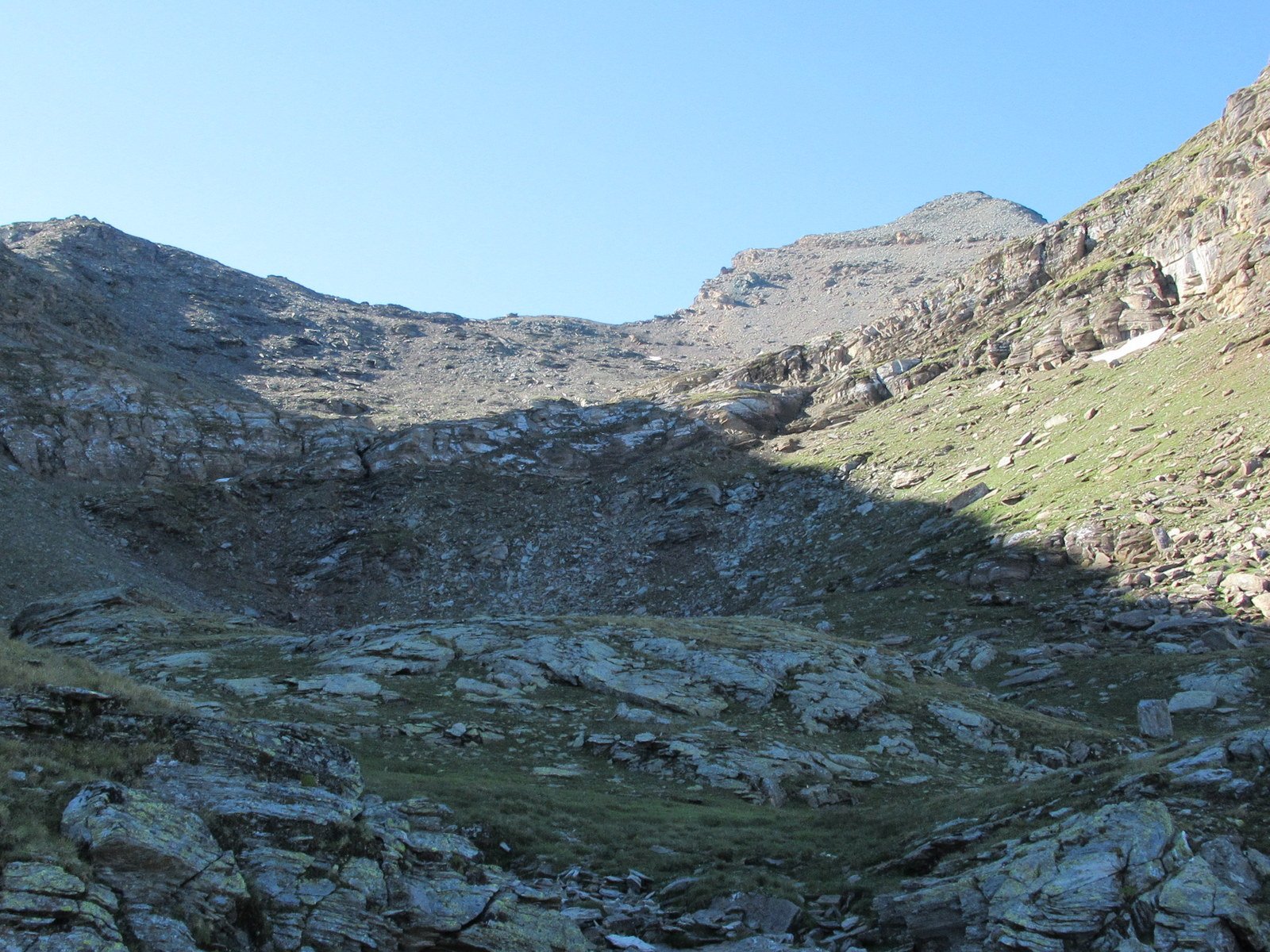 Il ripiano a monte del pendio erboso chiuso in fondo da una balza rocciosa, a dx la Punta Grand Revers