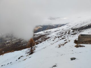 Dalla cima, quasi sull'orlo del pendio bianco sul fondo, al confine della zona innevata si scorgono le grange di Pian delle Stelle, sul punto di essere coperte dalla nuvola.