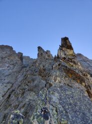Inizio del II tiro, doppiare la cresta a sinistra poi proseguire ascendendo per 10 mt, scalare una placca con passo di IV inf, poi puntare ad un torrione di pochi metri sostando alla sua destra.
